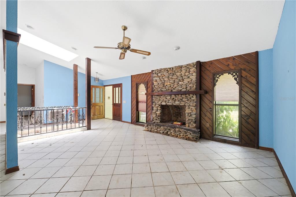 A living room features a stone fireplace, diagonal wood paneling, blue walls, and tiled flooring — 4444 RAINES ROAD, BROOKSVILLE, FL