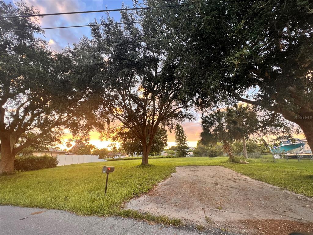 A grassy residential lot features a concrete driveway, mature trees, and a sunset sky — 550 E TARPON BOULEVARD NW, PORT CHARLOTTE, FL