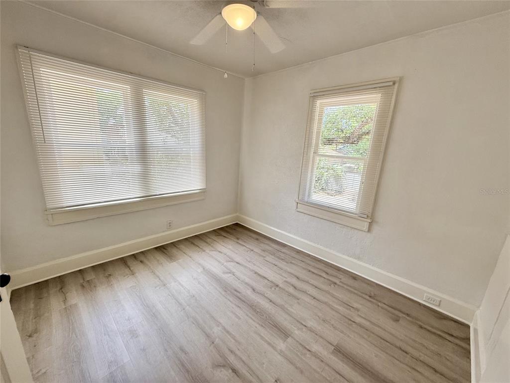 A bedroom features light wood-look flooring, white walls, two windows with blinds, and a ceiling fan — 1135 HIGHLAND STREET N UNIT 7, ST PETERSBURG, FL