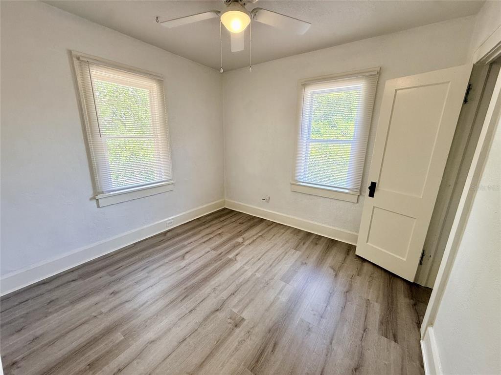 An empty bedroom features light-colored walls, wood-look flooring, two windows with blinds, and a ceiling fan — 1135 HIGHLAND STREET N UNIT 7, ST PETERSBURG, FL