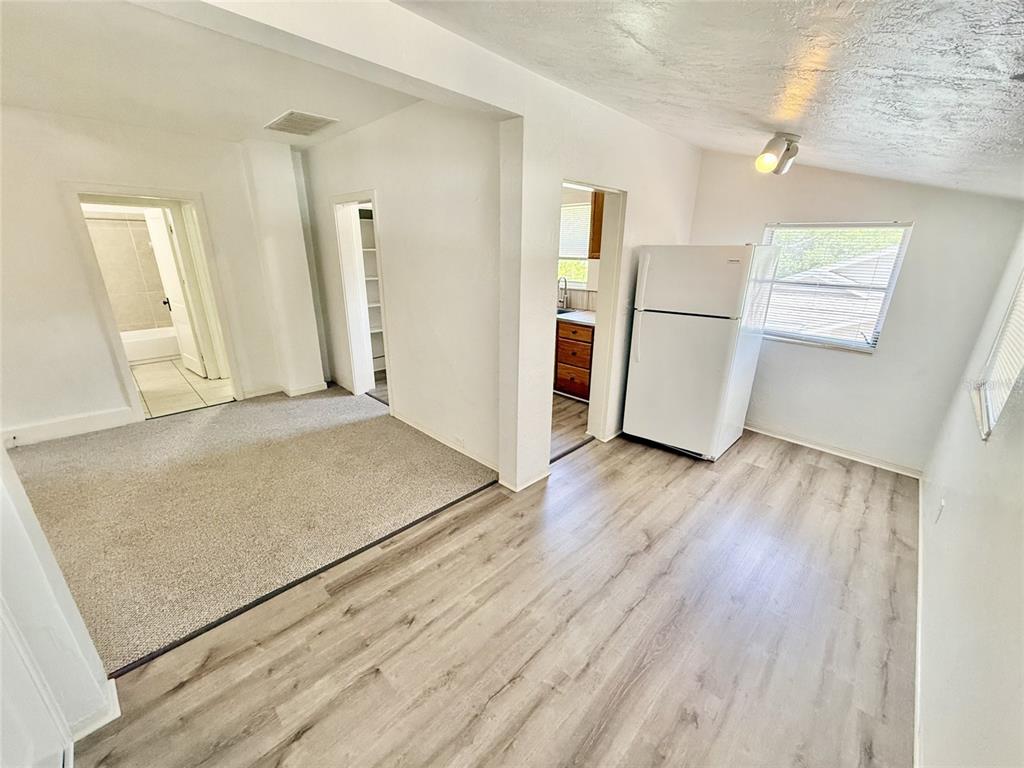 A room with light wood-look flooring, a white refrigerator, and an adjacent carpeted area — 1135 HIGHLAND STREET N UNIT 7, ST PETERSBURG, FL
