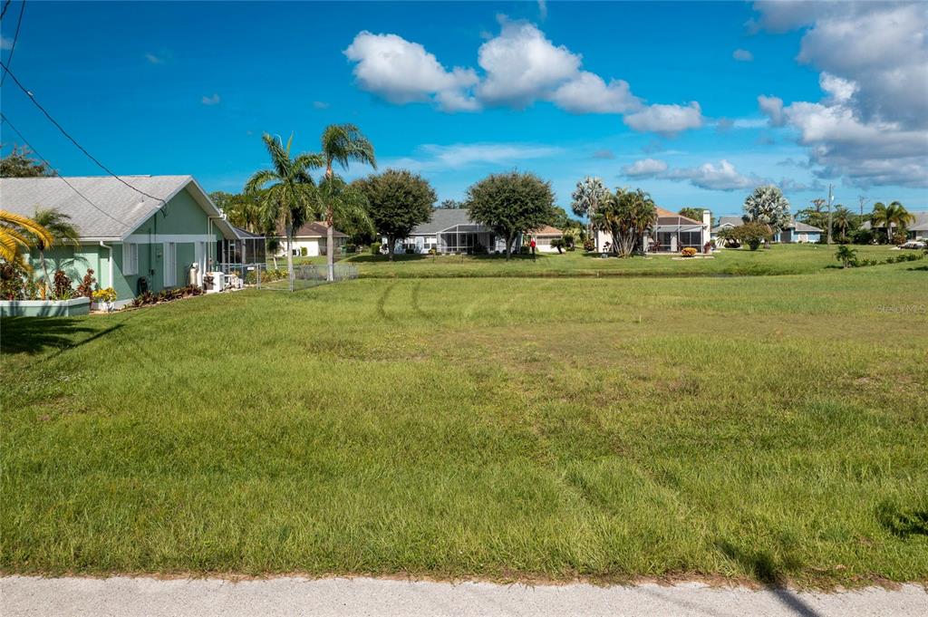 A vacant, grassy residential lot sits next to a light green house under a blue sky — 19 BUNKER TERRACE, ROTONDA WEST, FL
