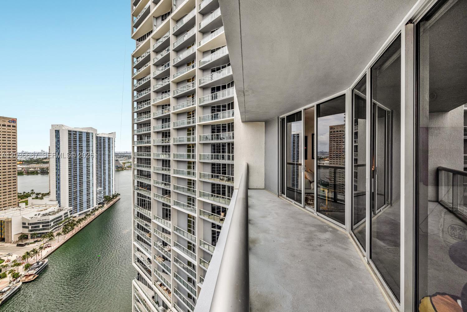 A high-rise balcony overlooks a canal and neighboring skyscrapers under a clear blue sky — 475 Brickell Ave # 3214, Miami FL 33131, MIAMI, FL