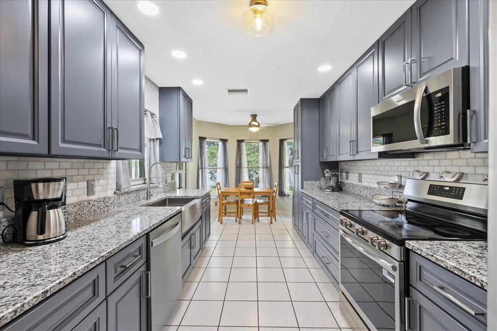 A galley kitchen features gray cabinets, granite countertops, stainless steel appliances, and a dining area — 8166 WINDING OAK LANE, SPRING HILL, FL