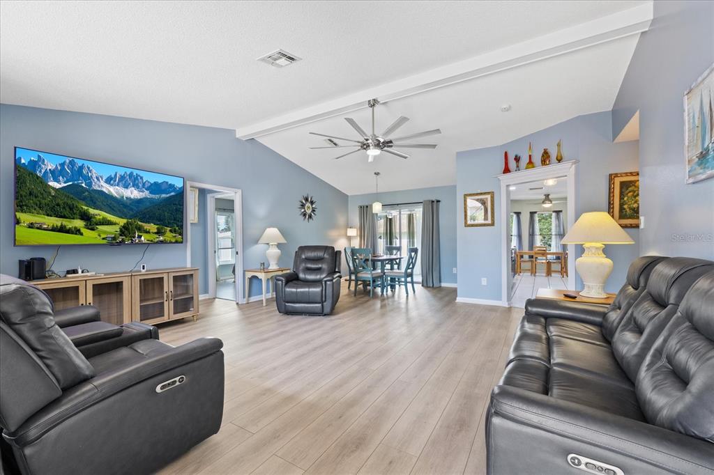 A spacious living room features light wood flooring, vaulted ceilings, and dark leather furniture — 8166 WINDING OAK LANE, SPRING HILL, FL