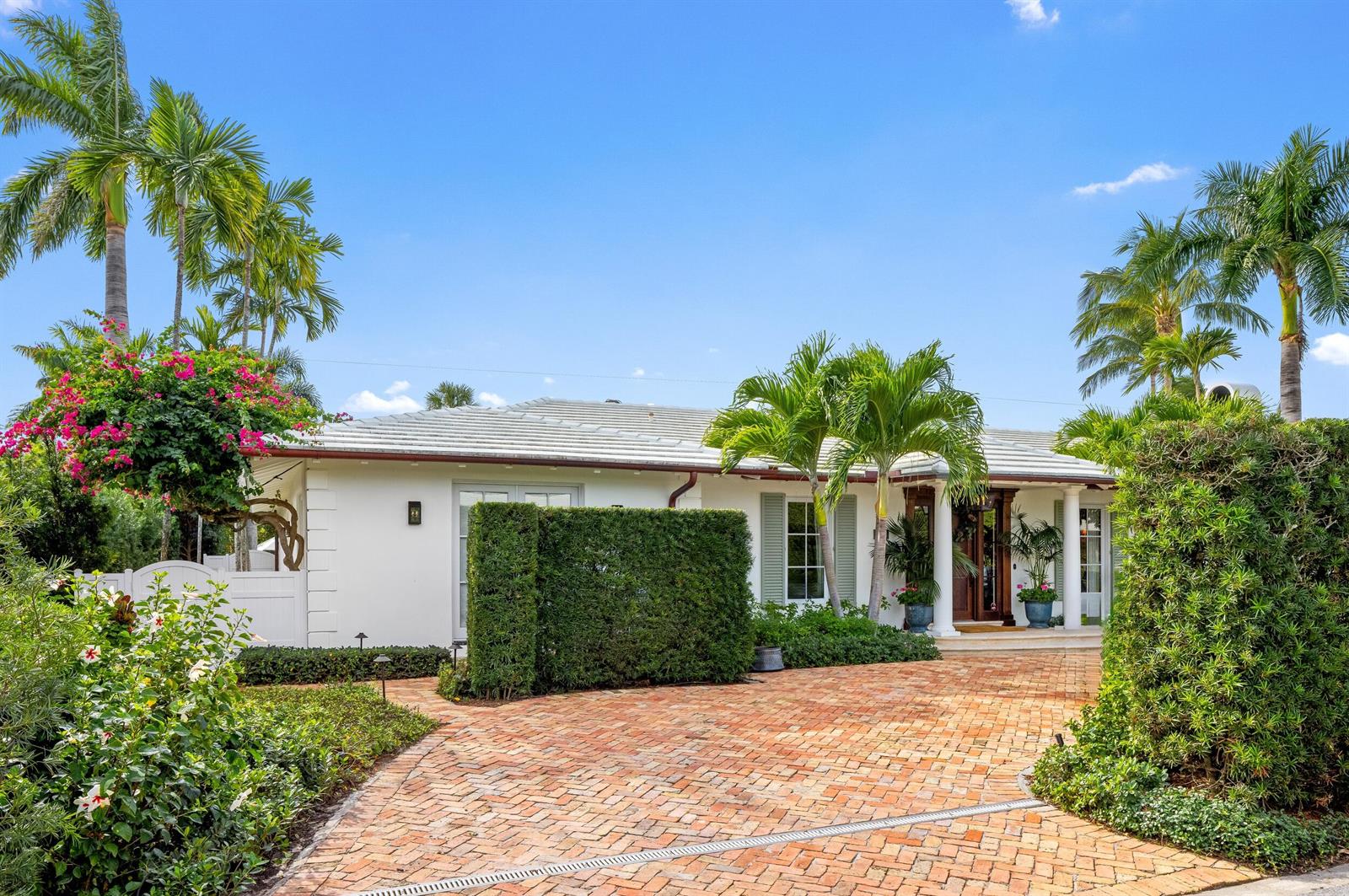 A white single-story house features a brick driveway, lush landscaping, and palm trees — 258 List Road, Palm Beach FL 33480, PALM BEACH, FL