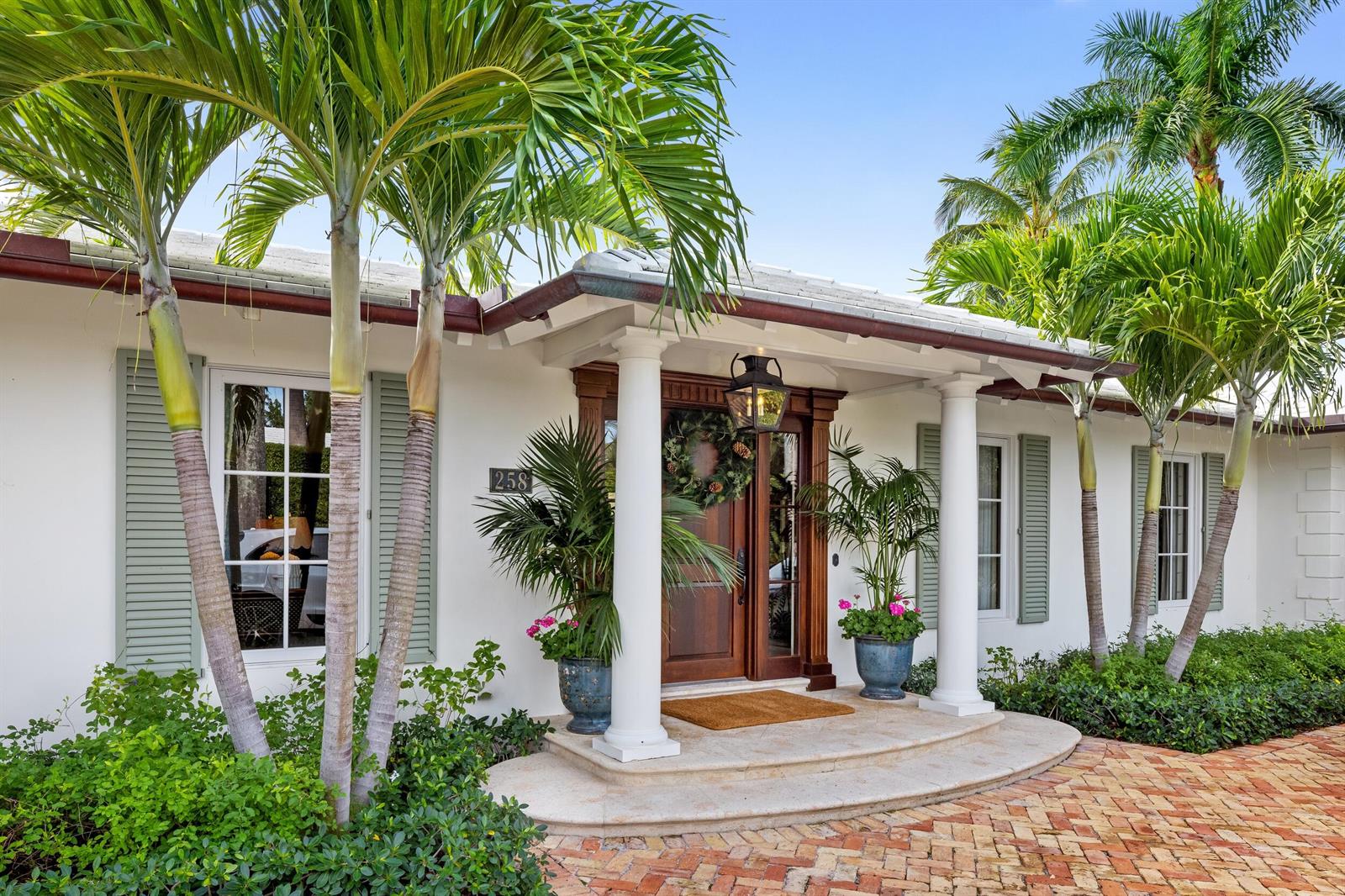 The exterior of a white house features a columned entryway, palm trees, and brick pavers — 258 List Road, Palm Beach FL 33480, PALM BEACH, FL