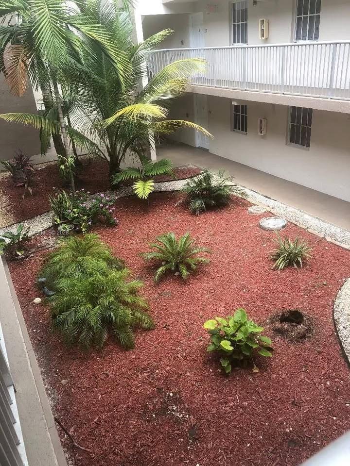 An elevated view of a courtyard garden with red mulch, palm trees, and small shrubs — 6155 NW 186th St # 209, Hialeah FL 33015, HIALEAH, FL