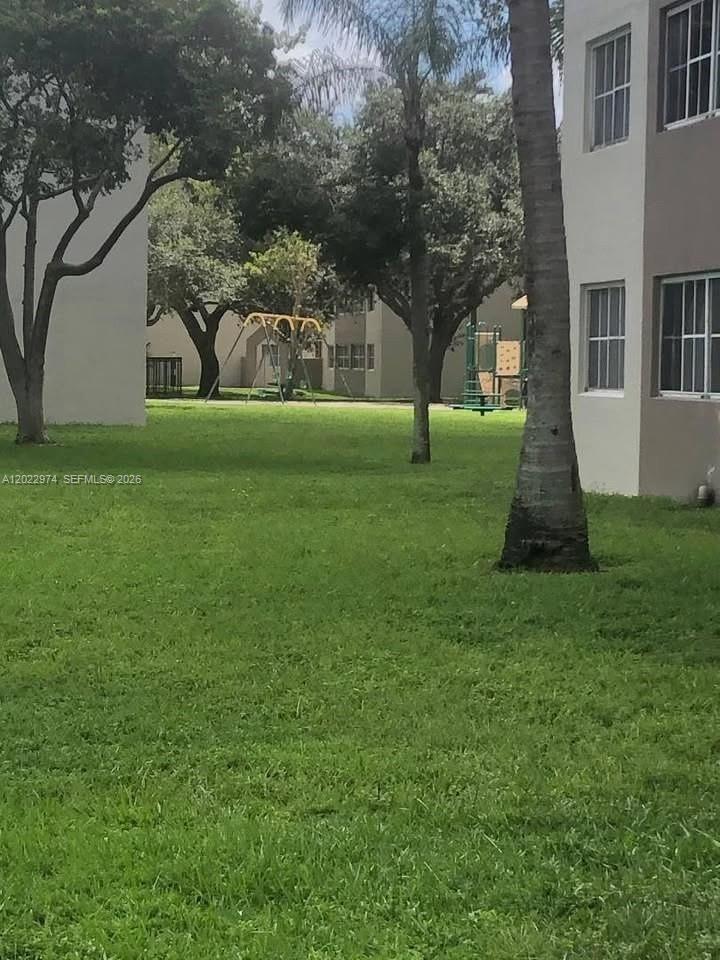 A grassy courtyard features a playground with a swing set between two apartment buildings — 6155 NW 186th St # 209, Hialeah FL 33015, HIALEAH, FL