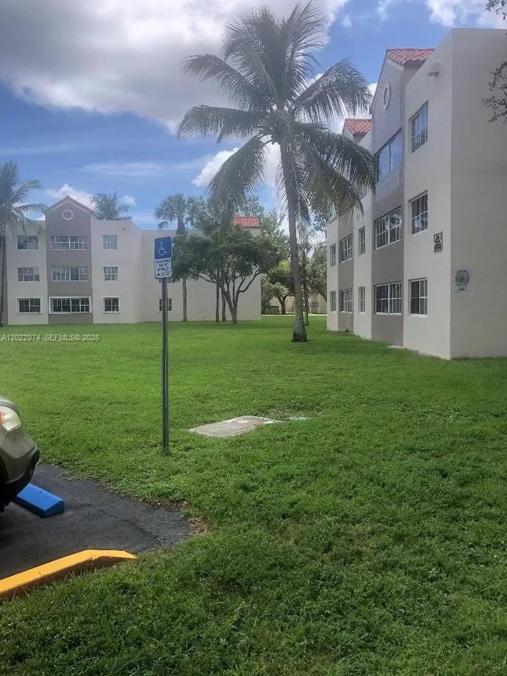 A grassy courtyard sits between two multi-story apartment buildings under a blue sky — 6155 NW 186th St # 209, Hialeah FL 33015, HIALEAH, FL