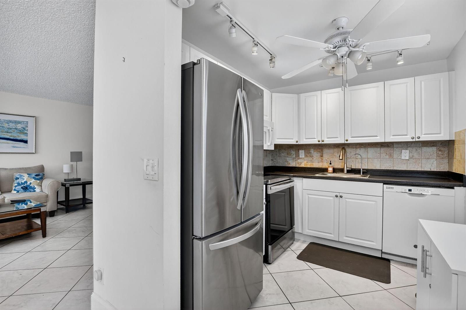 A kitchen with white cabinets, stainless steel appliances, and tile flooring opens to a living area — 739 Normandy P, Delray Beach FL 33484, DELRAY BEACH, FL