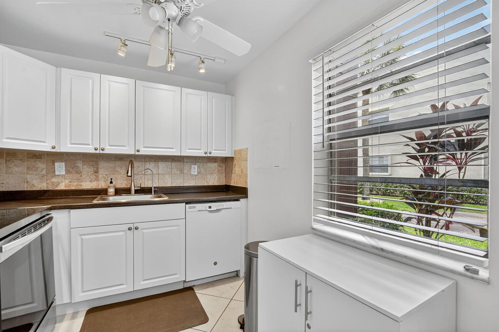 A kitchen features white cabinets, a dark countertop, a tile backsplash, and a window view — 739 Normandy P, Delray Beach FL 33484, DELRAY BEACH, FL