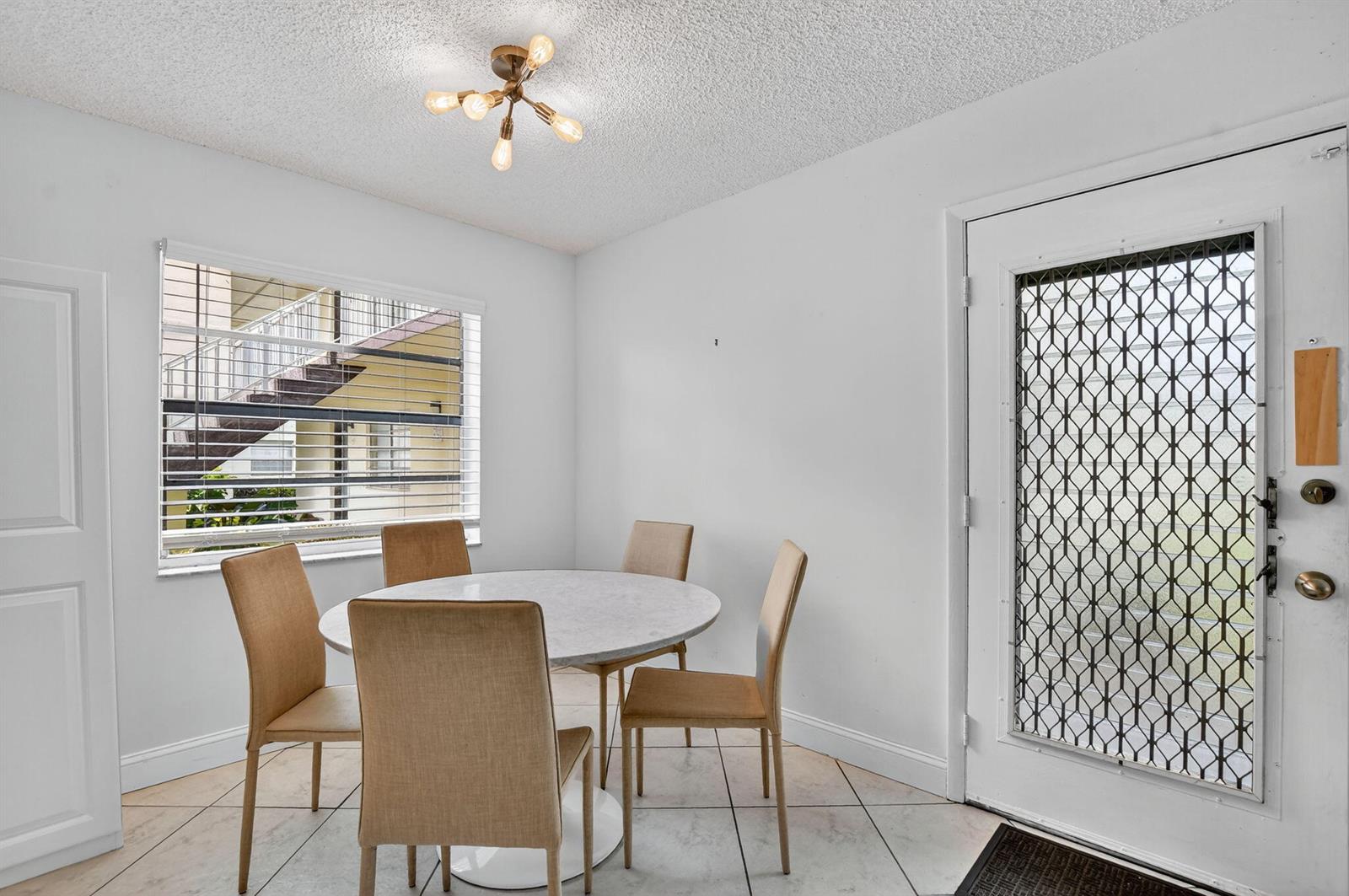 A dining area features a round marble table, four tan chairs, tile flooring, and a door — 739 Normandy P, Delray Beach FL 33484, DELRAY BEACH, FL