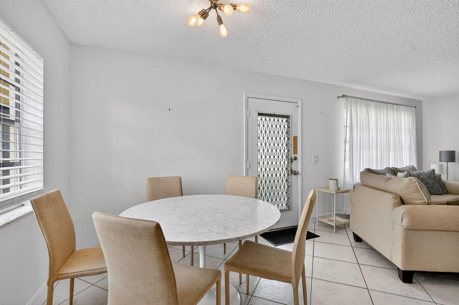 A dining area with a round marble table, four tan chairs, and a white door — 739 Normandy P, Delray Beach FL 33484, DELRAY BEACH, FL