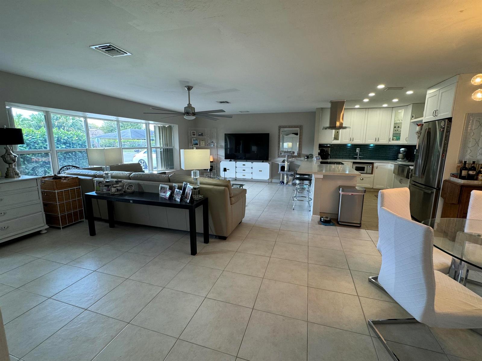 An open-concept living room and kitchen featuring tile flooring, white cabinetry, and large windows — 2099 S Conference Drive, Boca Raton FL 33486, BOCA RATON, FL