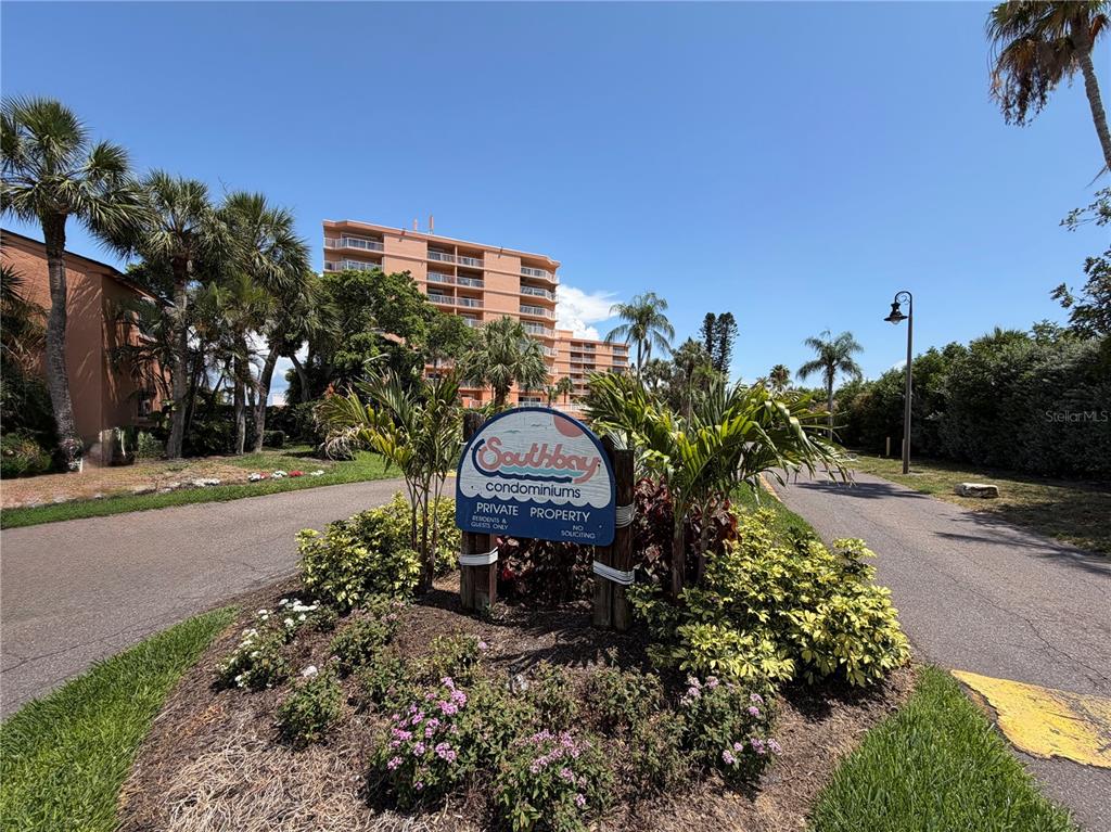 A sign for Southbay Condominiums stands in a landscaped island in front of a building — 7400 SUNSHINE SKYWAY LANE S UNIT 105, ST PETERSBURG, FL
