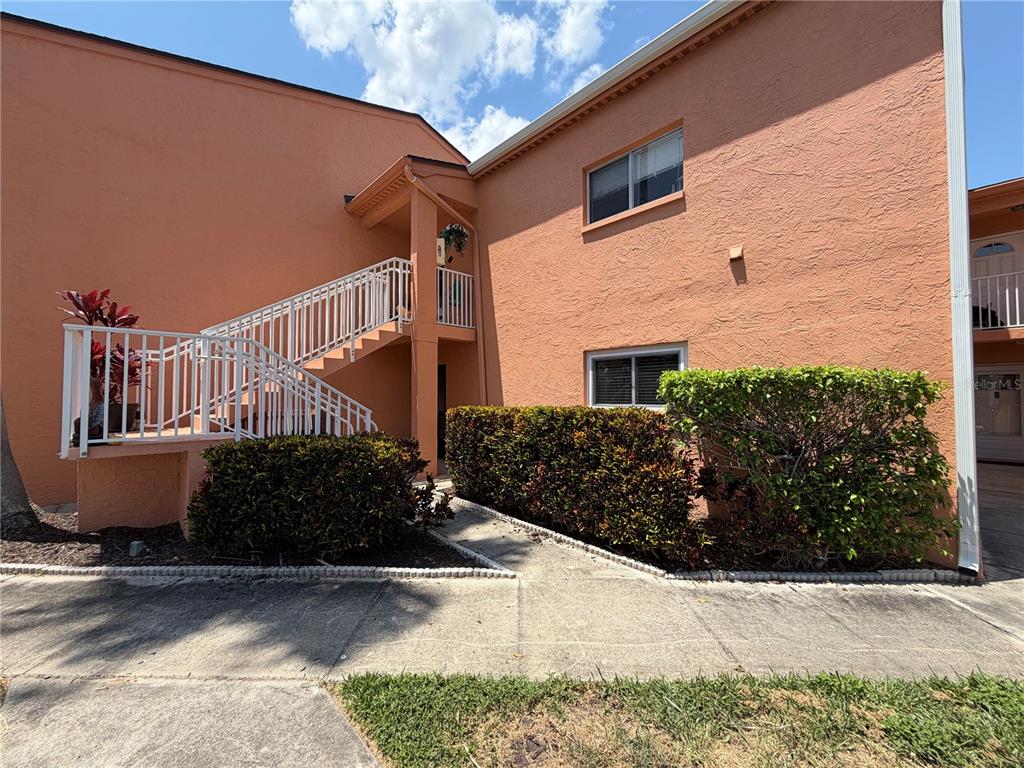 An exterior view of a two-story peach-colored apartment building with an outdoor staircase — 7400 SUNSHINE SKYWAY LANE S UNIT 105, ST PETERSBURG, FL