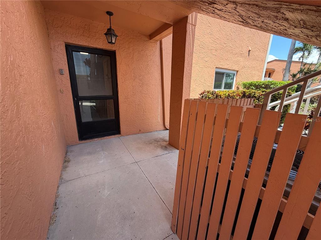 A concrete patio entrance features a black screen door and a wooden privacy fence — 7400 SUNSHINE SKYWAY LANE S UNIT 105, ST PETERSBURG, FL