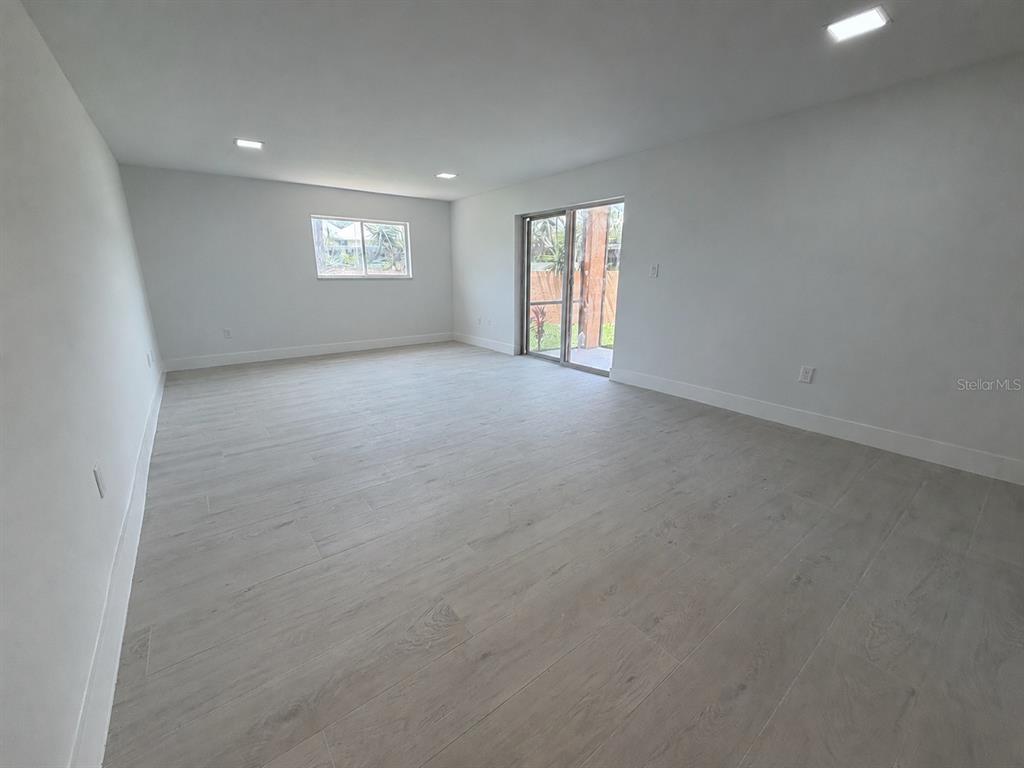 A spacious, empty room features light-colored wood-look tile flooring, white walls, and sliding glass doors — 7400 SUNSHINE SKYWAY LANE S UNIT 105, ST PETERSBURG, FL