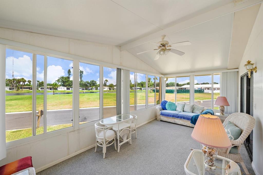 A sunroom with carpeted floors, a ceiling fan, and large windows overlooking a grassy field — 132 LAKEVIEW DRIVE UNIT 132, PALMETTO, FL
