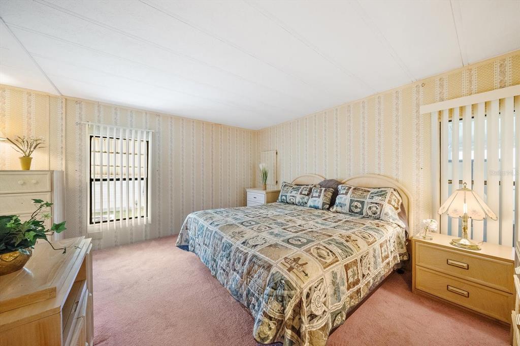 A bedroom features striped wallpaper, pink carpeting, a patterned bedspread, and two windows with blinds — 132 LAKEVIEW DRIVE UNIT 132, PALMETTO, FL