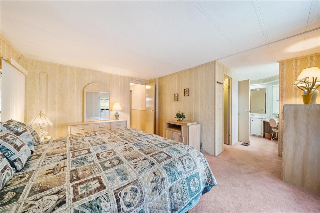 A bedroom with wood-paneled walls, pink carpet, a patterned quilt, and an attached bathroom — 132 LAKEVIEW DRIVE UNIT 132, PALMETTO, FL