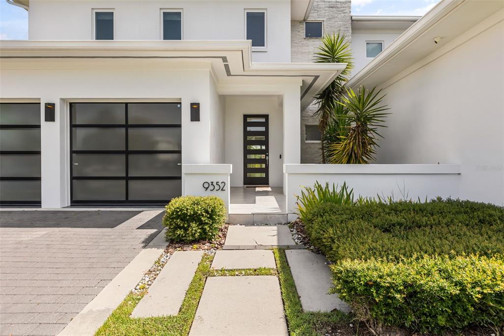 The exterior of a modern white house features a dark garage door and front entrance — 9352 BORDET COURT, ORLANDO, FL
