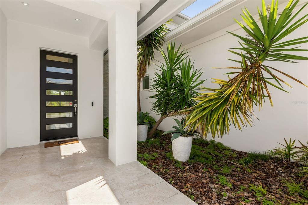 A modern entryway features a dark front door, tiled flooring, and a landscaped garden bed — 9352 BORDET COURT, ORLANDO, FL