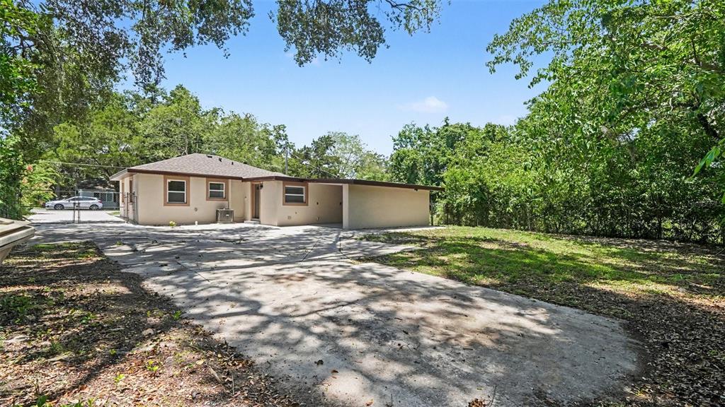 A single-story house with a carport and a large concrete driveway surrounded by trees — 1109 NW 14TH AVENUE, OCALA, FL