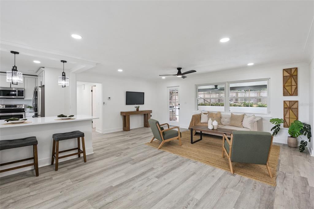 An open-concept living room and kitchen featuring light wood floors, white walls, and neutral furniture — 1510 OVERLOOK DRIVE, MOUNT DORA, FL
