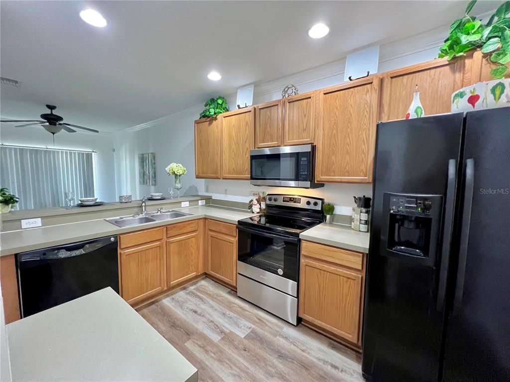 A kitchen features wood cabinets, stainless steel appliances, a black refrigerator, and a sink island — 12425 FOXMOOR PEAK DRIVE, RIVERVIEW, FL
