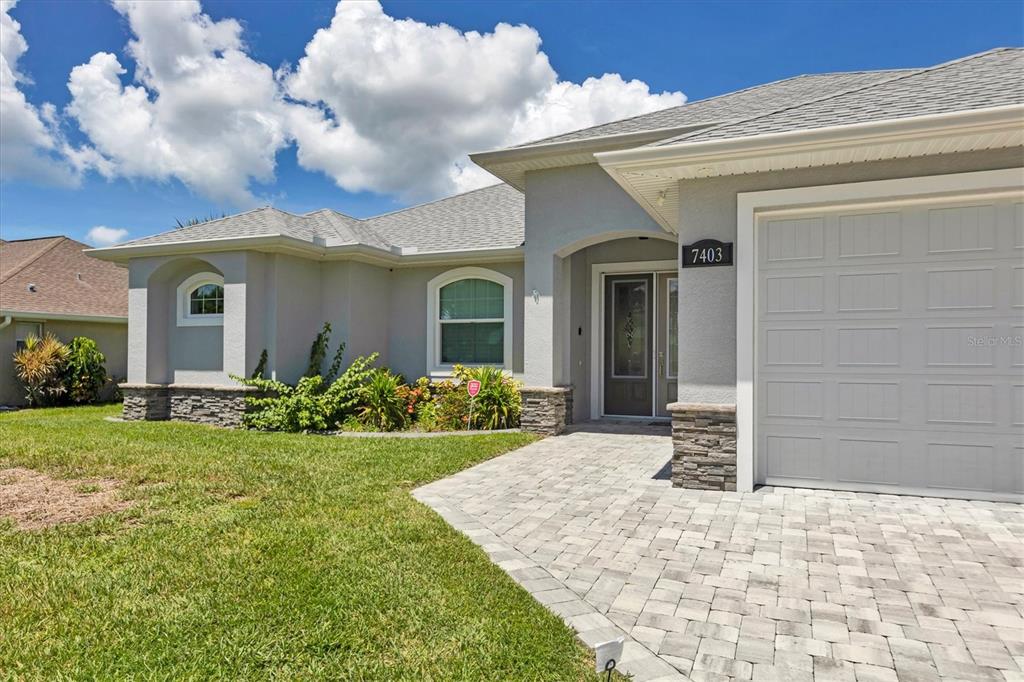 A single-story house with a gray stucco exterior, stone accents, and a paved driveway — 7403 SNOW DRIVE, ENGLEWOOD, FL