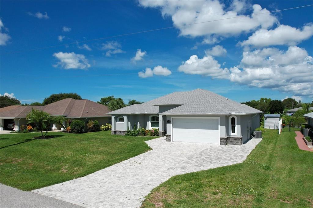 A gray single-story house with a white garage door and a paved driveway under blue skies — 7403 SNOW DRIVE, ENGLEWOOD, FL