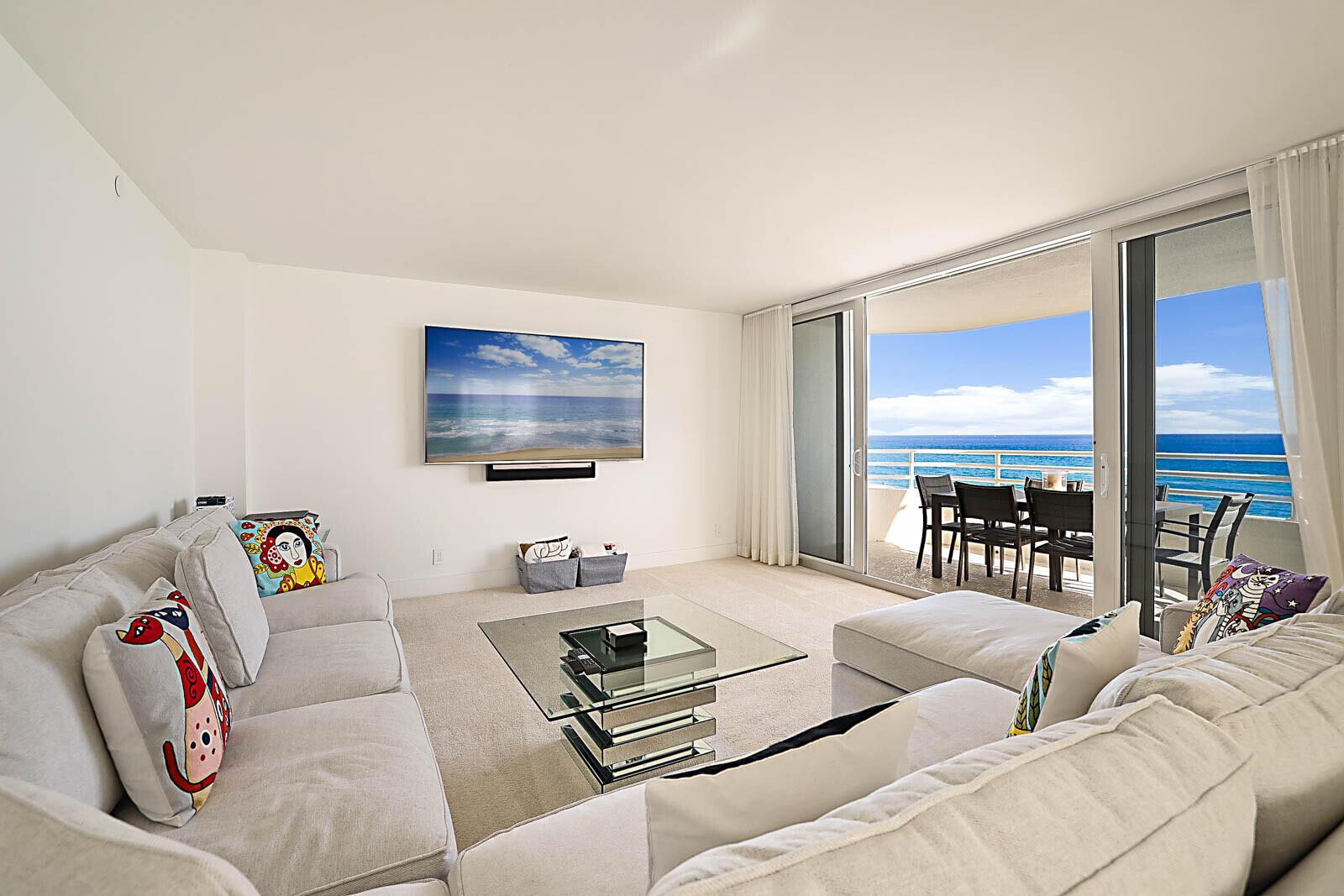 A living room with a sectional sofa, glass coffee table, wall-mounted television, and balcony ocean views — 3407 S Ocean Boulevard # 8a, Highland Beach FL 33487, HIGHLAND BEACH, FL