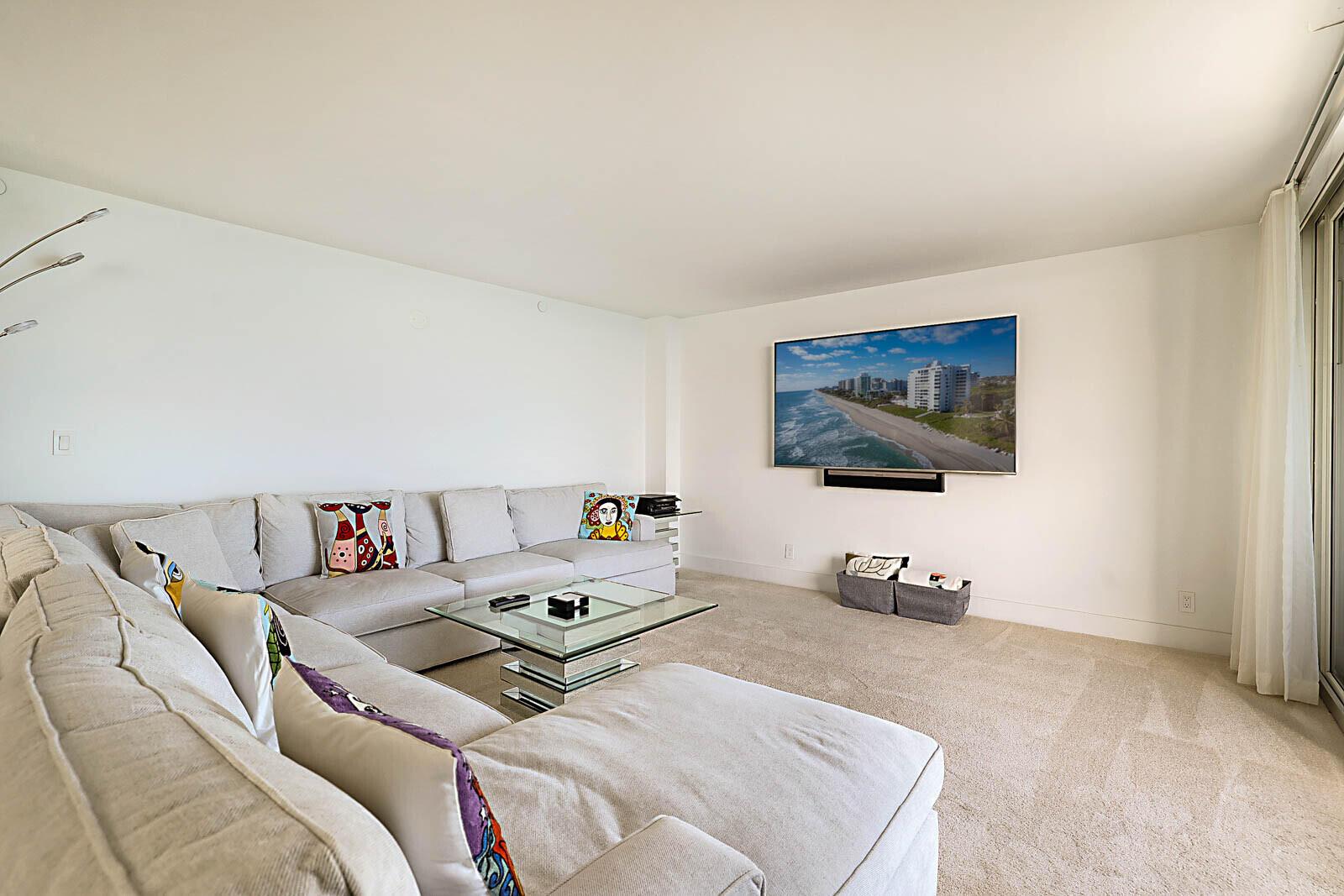 A living room features a large sectional sofa, a glass coffee table, and a wall-mounted television — 3407 S Ocean Boulevard # 8a, Highland Beach FL 33487, HIGHLAND BEACH, FL