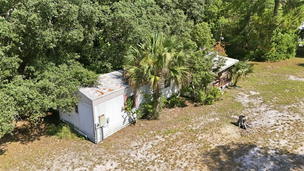 An aerial view of a weathered mobile home surrounded by trees and sandy ground — 37807 DEERWOODS DRIVE, EUSTIS, FL