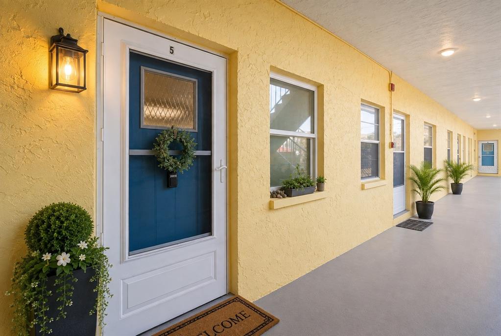 A yellow exterior hallway features a row of blue doors with white frames and plants — 9895 1ST STREET E UNIT 5, TREASURE ISLAND, FL