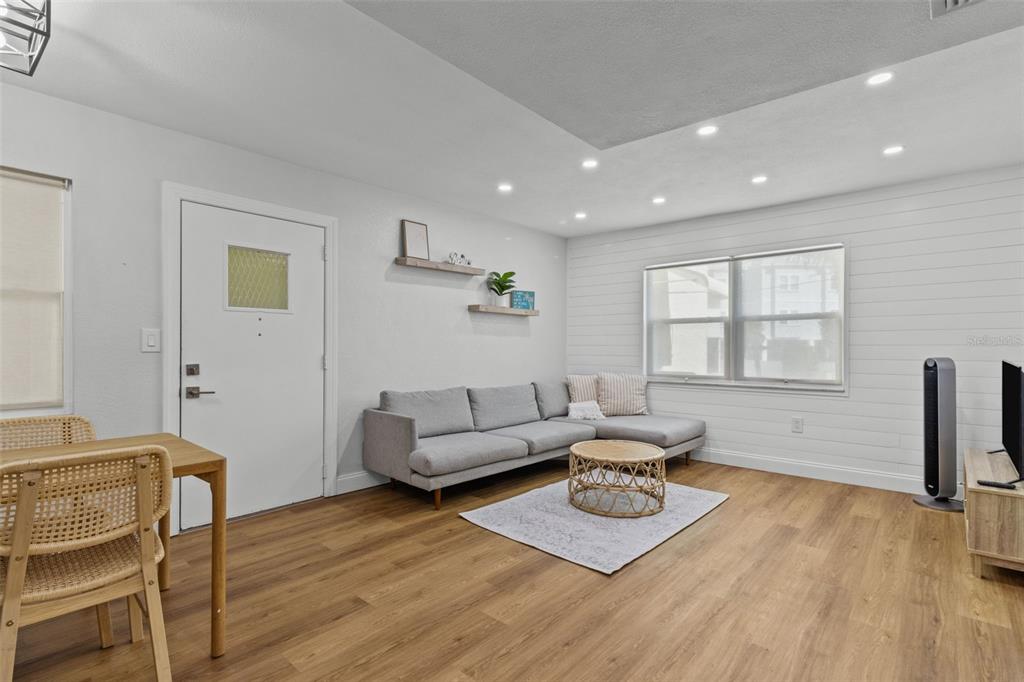 A living room features light wood flooring, a grey sectional sofa, and white shiplap walls — 9895 1ST STREET E UNIT 5, TREASURE ISLAND, FL