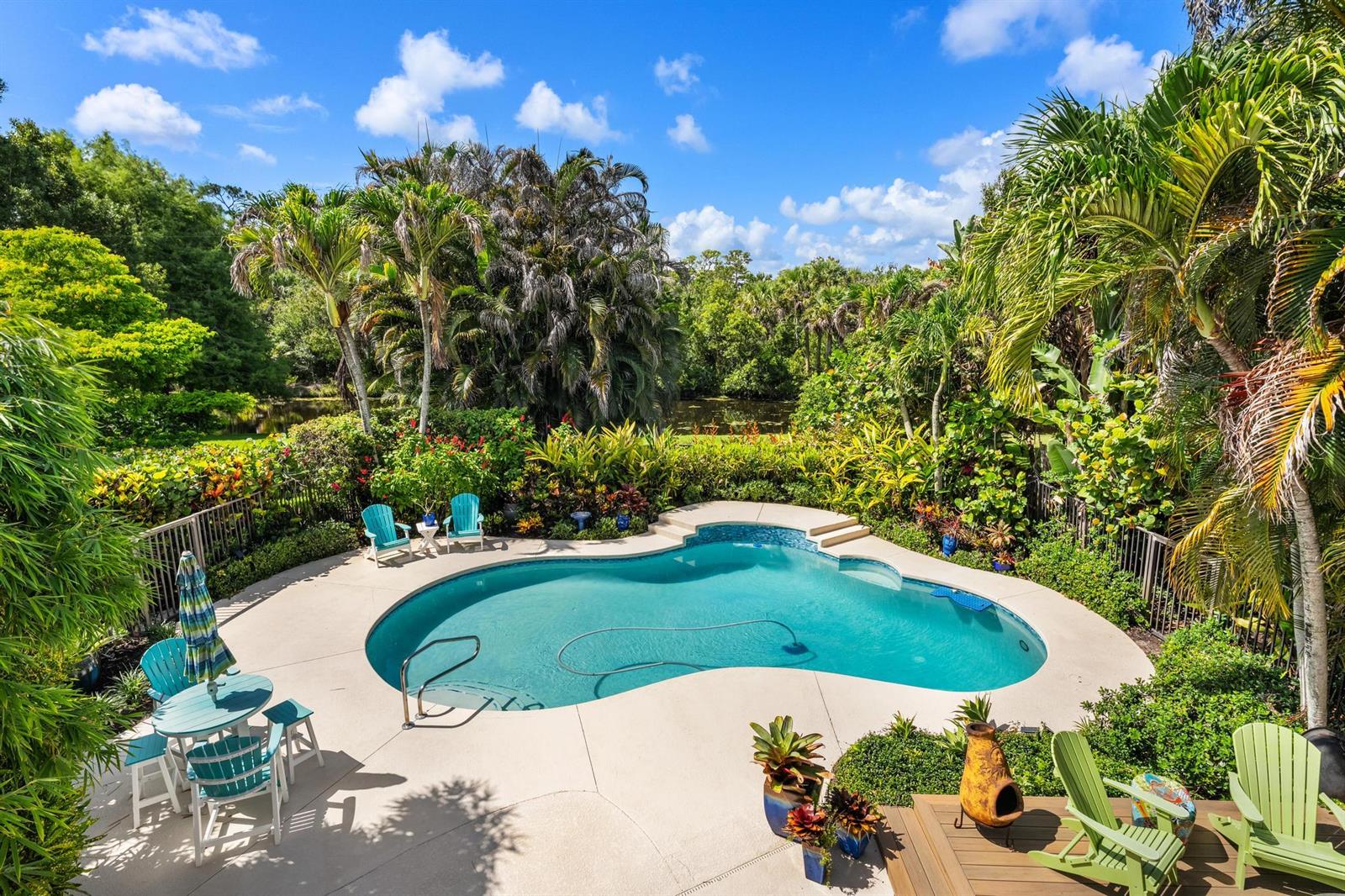 A kidney-shaped swimming pool sits on a patio surrounded by lush tropical landscaping and trees — 19646 Red Maple Lane, Jupiter FL 33458, JUPITER, FL