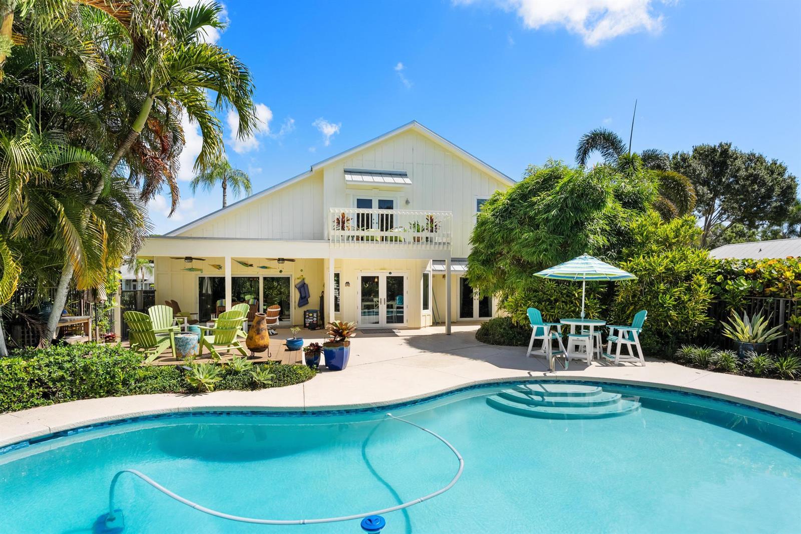 A yellow two-story house features a backyard swimming pool, patio, and lush tropical landscaping — 19646 Red Maple Lane, Jupiter FL 33458, JUPITER, FL