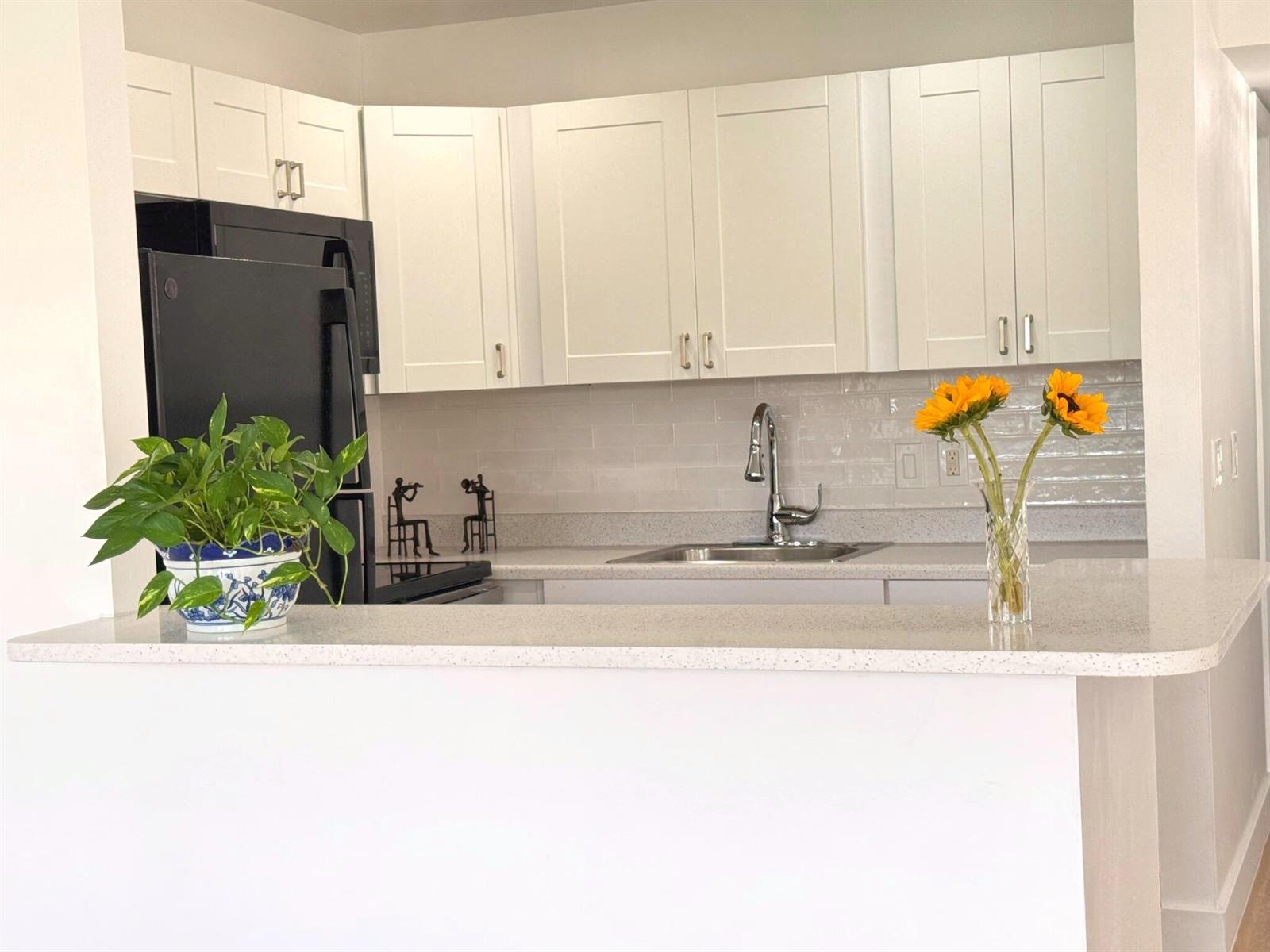 A kitchen features white shaker cabinets, a black refrigerator, a light countertop, and a backsplash — 150 Windsor G, West Palm Beach FL 33417, WEST PALM BEACH, FL