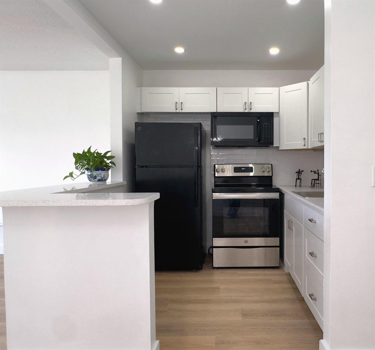 A kitchen features white cabinets, stainless steel appliances, a black refrigerator, and light wood flooring — 150 Windsor G, West Palm Beach FL 33417, WEST PALM BEACH, FL