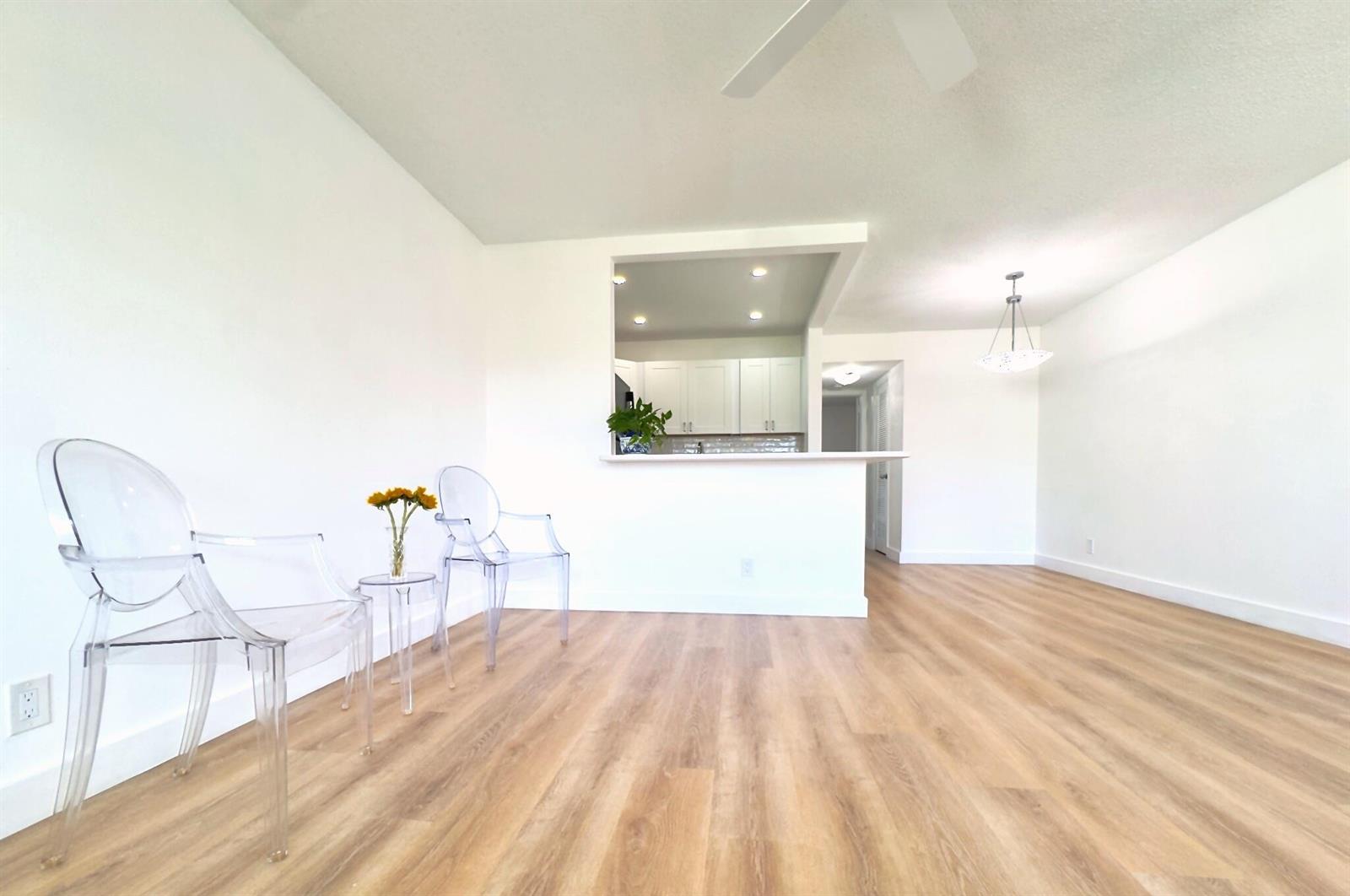 A bright living room with light wood flooring, white walls, and two clear plastic chairs — 150 Windsor G, West Palm Beach FL 33417, WEST PALM BEACH, FL