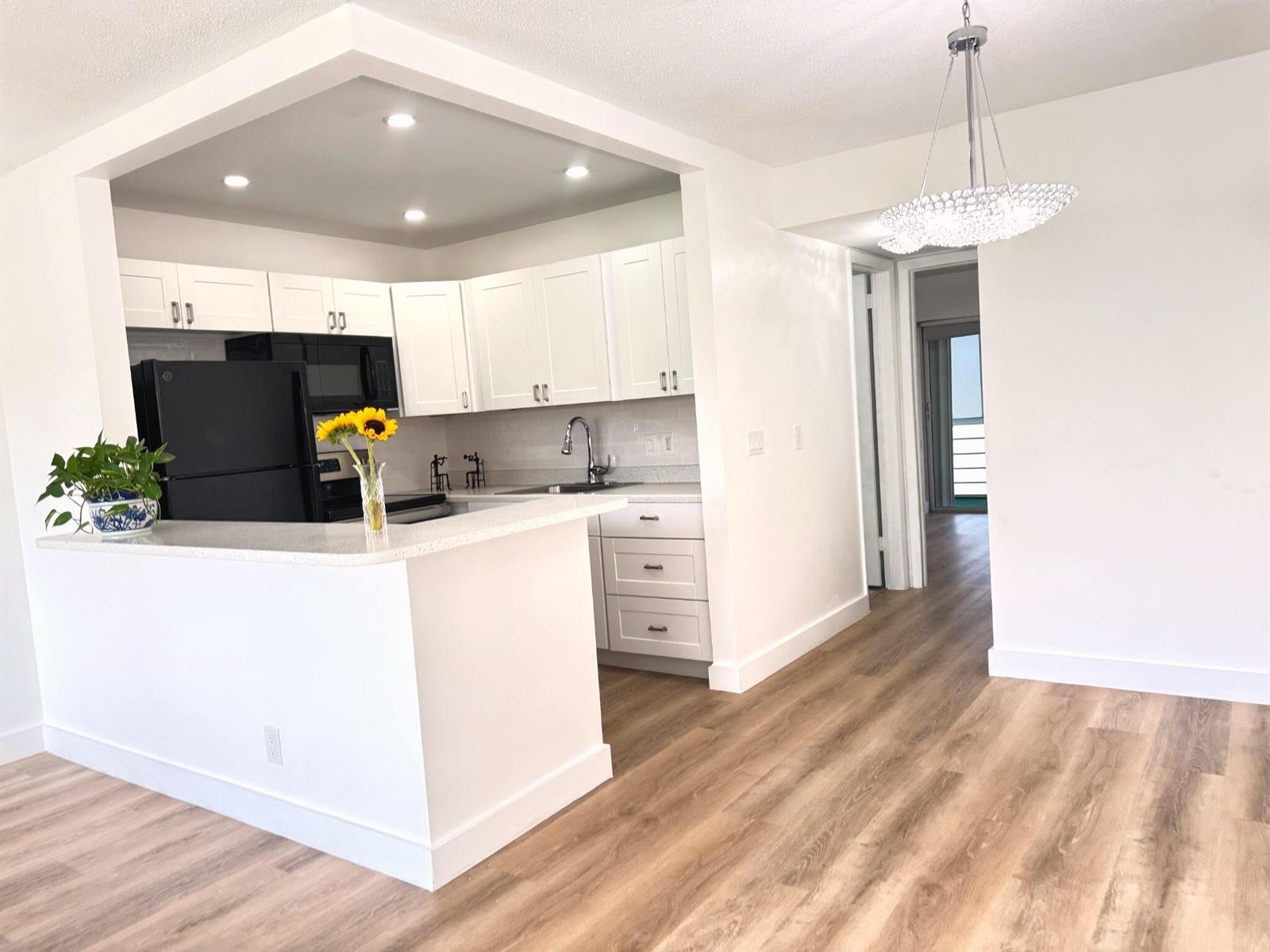 A white kitchen with black appliances, light countertops, and wood-look flooring opens to a dining area — 150 Windsor G, West Palm Beach FL 33417, WEST PALM BEACH, FL