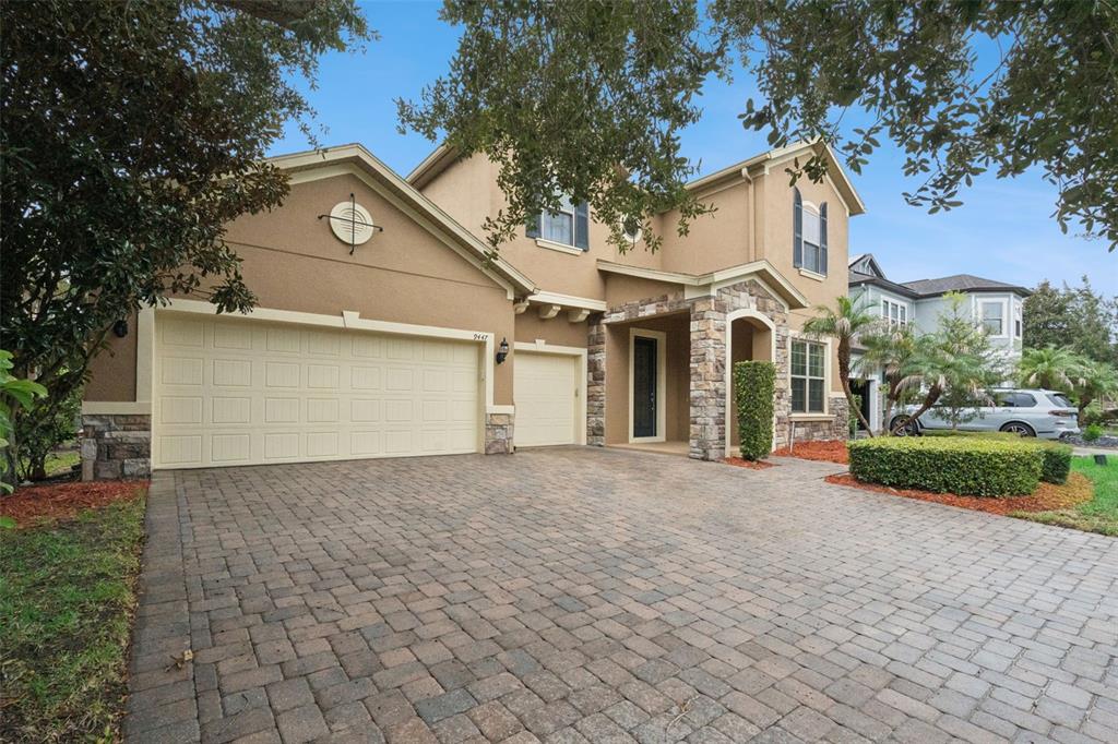 A two-story house with a tan stucco exterior, stone accents, and a paved driveway — 9447 PRINCE HARRY DRIVE, ORLANDO, FL