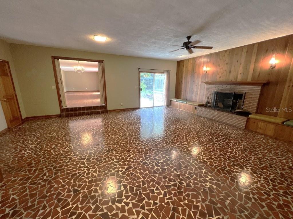 A living room features a stone-tiled floor, a wood-paneled fireplace wall, and sliding glass doors — 106 SW 38TH STREET, GAINESVILLE, FL