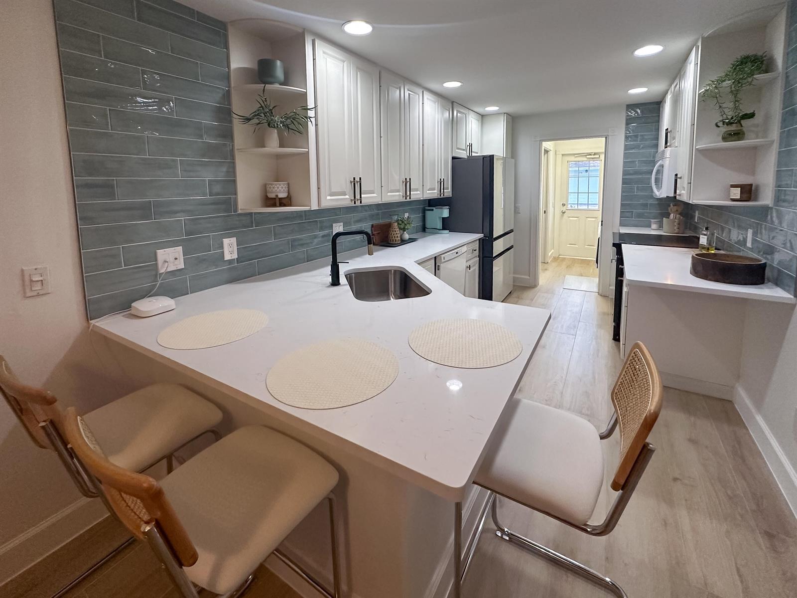 A kitchen features white cabinets, a quartz peninsula, and blue subway tile backsplashes — 3032 W Community Drive, Jupiter FL 33458, JUPITER, FL