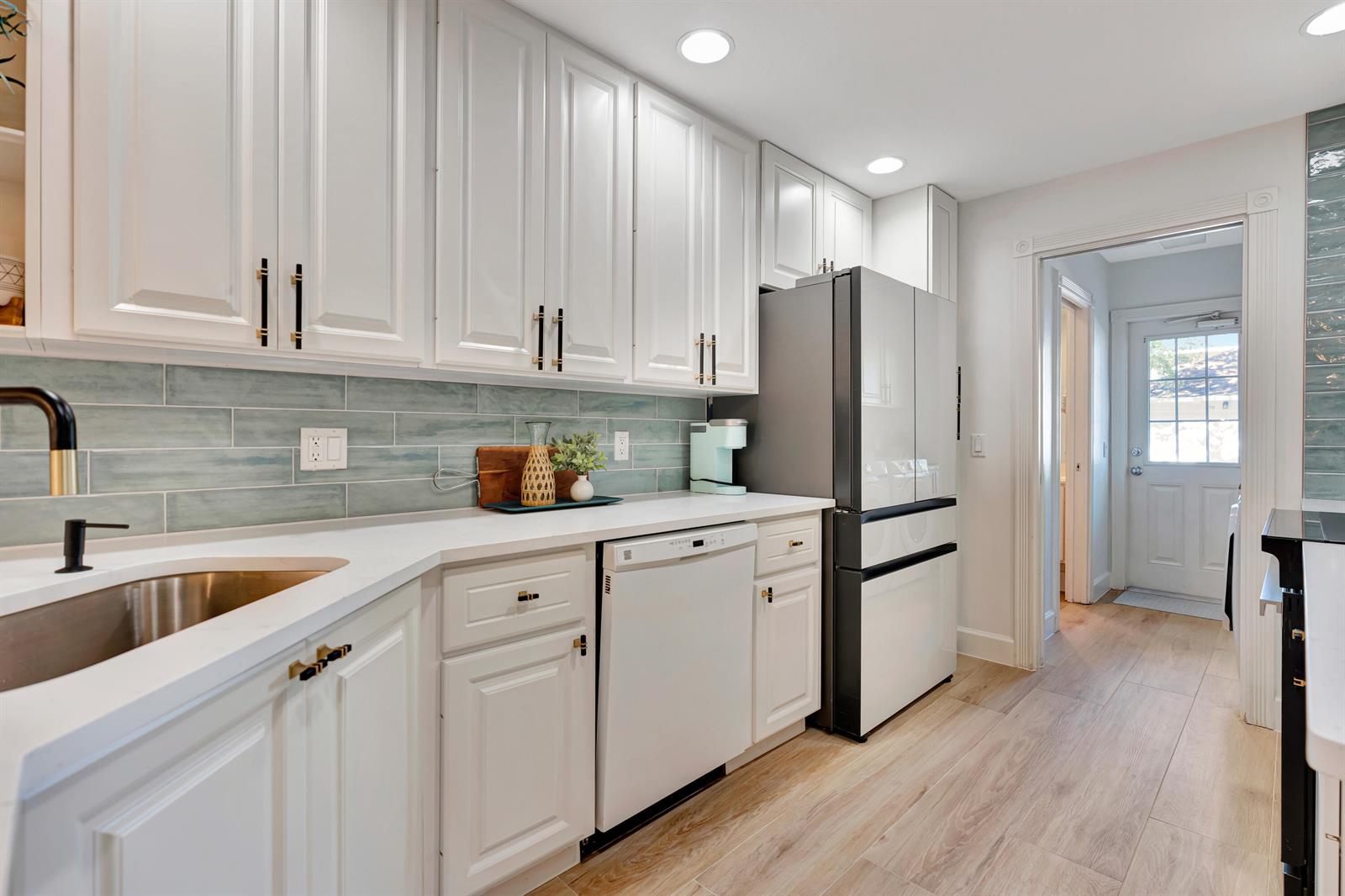 A kitchen features white cabinets, light blue subway tile backsplash, stainless appliances, and wood-look flooring — 3032 W Community Drive, Jupiter FL 33458, JUPITER, FL