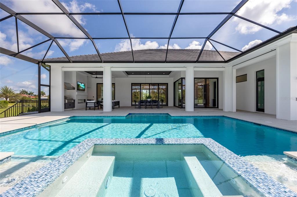A swimming pool and spa sit under a screened lanai with an outdoor kitchen area — 15850 HAMPTON VIEW COURT, FORT MYERS, FL