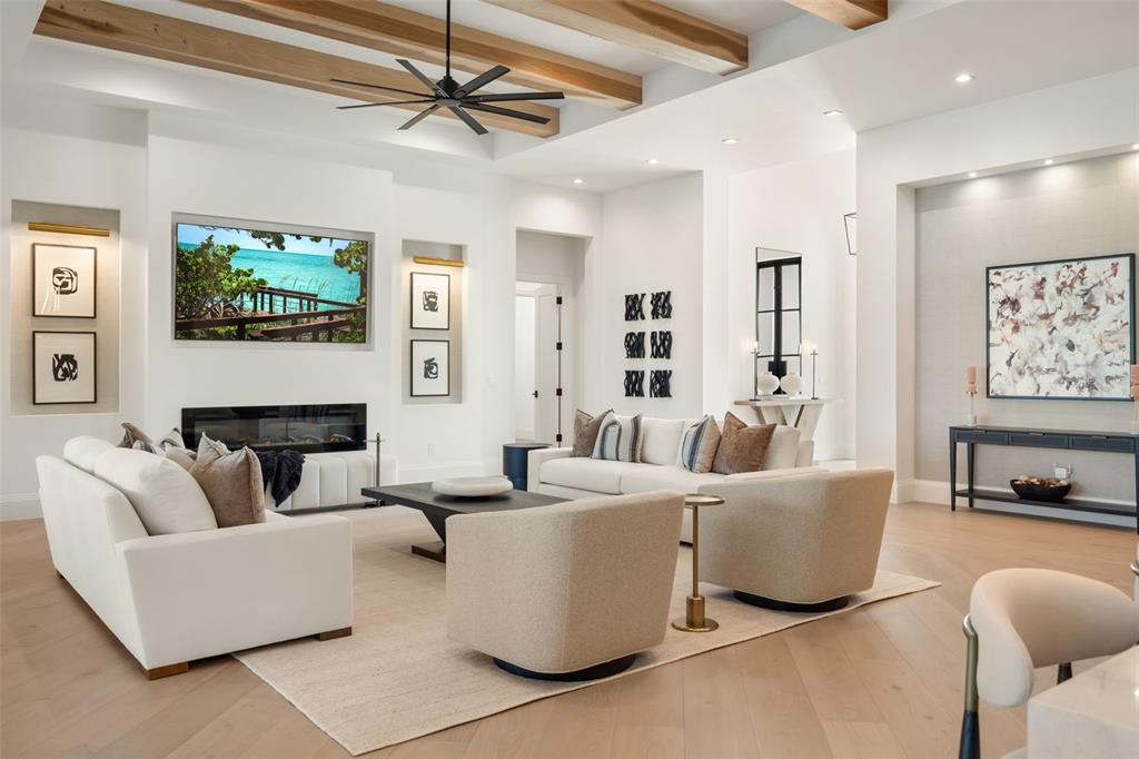 A modern living room features white sofas, a fireplace, wood ceiling beams, and neutral decor — 15850 HAMPTON VIEW COURT, FORT MYERS, FL